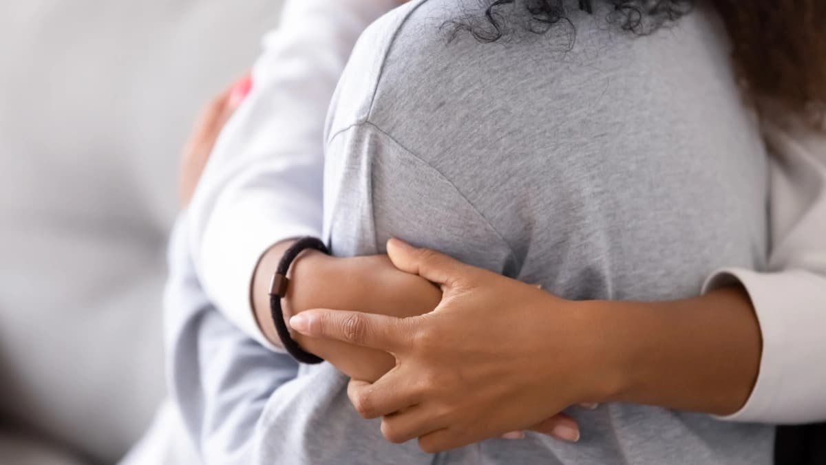 Close-up photograph of woman's hands wrapped around a person she is holding close.